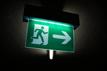 Green wall mounted illuminated exit sign in a dark underground parking, no people