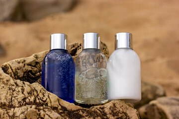 Fototapeta na wymiar Plastic bottles with natural cosmetic in travel containers - blue shower gel, shampoo with bubbles inside, body lotion in miniature containers against a brown stone rock background. Face body care.