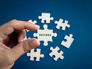 Success concept. Word "SUCCESS" showing on puzzle jigsaw piece holding by business person's hand, choosing from other pieces on blue background.