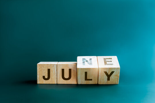 Changing the month of mid of the year. Flipping wooden cube blocks for change words, months from June to July, isolated on blue background with copy space, clean, modern, and minimal style.