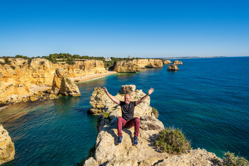 Happy man sitting on the top of cliffs at Marinha beach, Algarve, Portugal