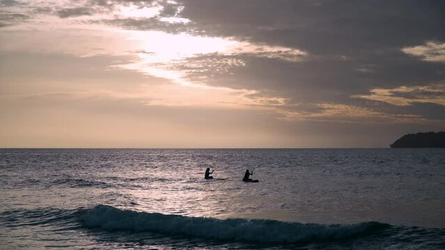 Two Women Rowing Sitting on Paddleboards Against Sunset Over the Sea. SUP Near Tanjung Aru Beach, Kota Kinabalu, Malaysia