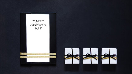 Father's Day. black envelope mockup, shot from the top on a black background with copy space. Tied with a gold ribbon. Three Gift boxes with ribbon. white blank card for text. Business invitation