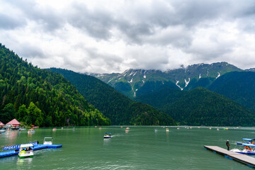Fototapeta na wymiar Alpine Lake Ritsa. Tourists on catamaran sailing along lake among mountains.