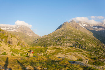 Golden hour in a green mountain landscape in summer, a hiking trail is going through the valley to the Mount Cenis Lake in the Alps. The sky is blue and the clouds are soft.