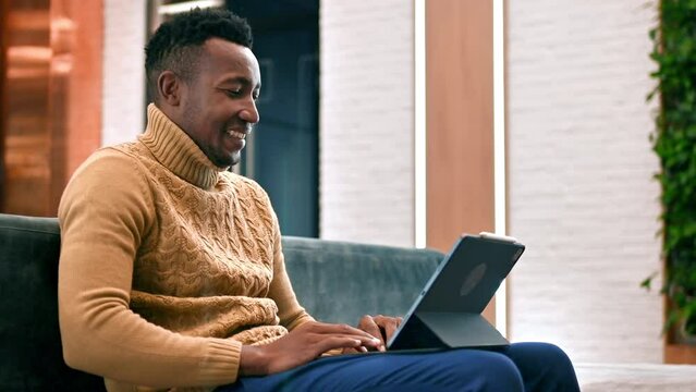 Black man working using a tablet while sitting on a sofa in an office. Slow motion
