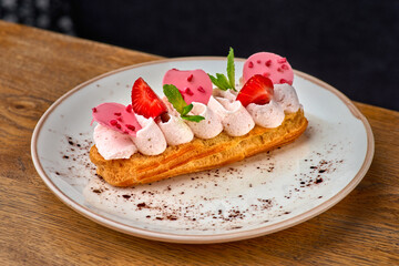 Eclairs with cream and strawberries on a white plate