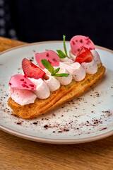 Eclairs with cream and strawberries on a white plate