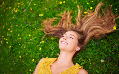 Appreciating the beauty of life. High angle shot of a carefree young woman relaxing in a field of grass and flowers.