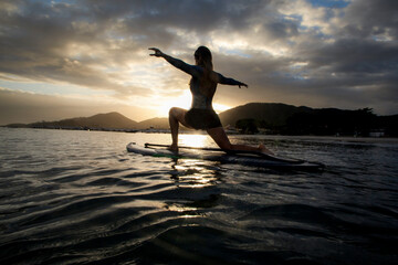 Woman with open arms over stand Up paddle at sunrise, Brazilian beach