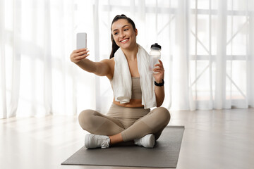 Fototapeta na wymiar Happy sporty lady taking selfie after workout indoors, using phone