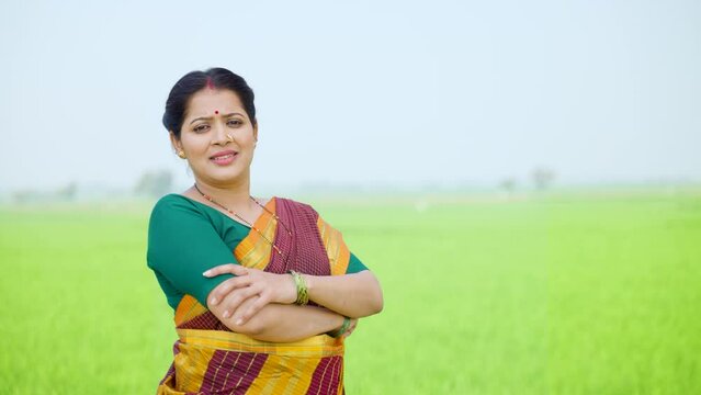 Confident village woman standing with crossed arms by looking camera at agriculture farmland - concept of successful agribusiness, determination and empowerment.