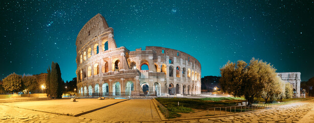 Fototapeta na wymiar Rome, Italy. Colosseum Also Known As Flavian Amphitheatre In Evening Or Night Time. Travel Italy. Bright Blue Night Sky. Amazing Night Starry Sky Background. Panoramic View.