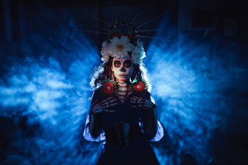 Woman with mexican skull halloween makeup in dark with backlight rays. Day of the dead aka Dia de los Muertos and halloween concept.