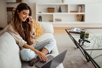 Happy busy young asian woman calling by smartphone, typing on computer