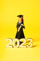 Class of 2023 concept. Wooden number 2023 with graduate statuette on color background