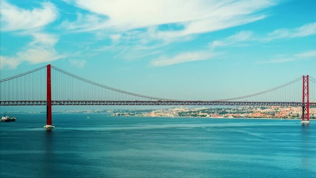 Timelapse of 25 de Abril Bridge famous tourist landmark of Lisbon connecting Lisboa to Almada on Setubal Peninsula over Tagus river with boats yachts and vessels moving. Lisbon, Portugal. Camera pan