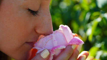 Horizontal portrait of a young woman enjoying the smell of a rose flower