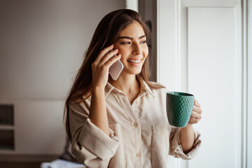 Happy young pretty asian woman calling by phone, talking, enjoy cup of drink in free time