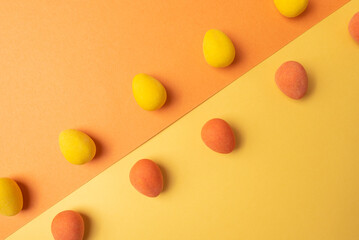 Background of yellow and orange egg-shaped candies on opposite sides color surfaces, on a diagonal line.