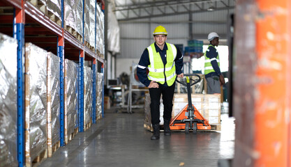 Warehouse worker pulling manual pallet hand truck loaded stack of merchandise in cardboard boxes....