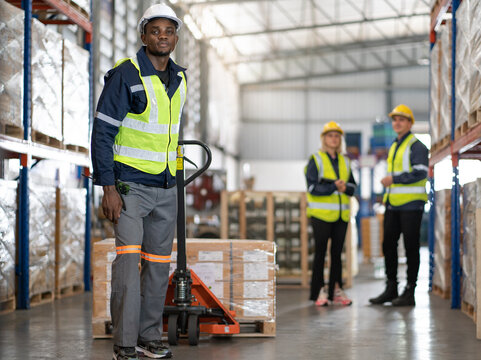 Warehouse worker pulling manual pallet hand truck loaded stack of merchandise in cardboard boxes. Multiracial store worker walking in distribution shipping factory with cargo on hand truck. copy space