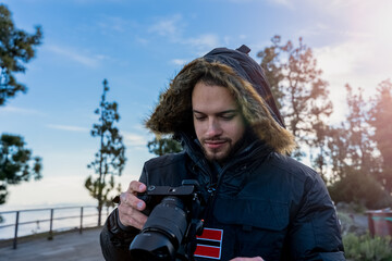 turista observando fotos en cámara de fotografía mirrorless sonriendo, con chaqueta de invierno 