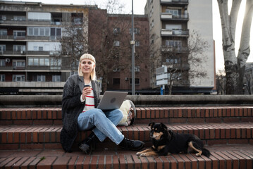 Young university girl sitting outdoor with her adopted dog working on laptop. She left the apartment for her student roommate boyfriend they need privacy because they share a rented apartment or room