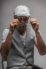 Young handsome man wearing gray cap and vest trying on glasses