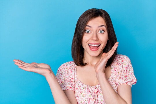 Photo portrait of lovely young woman palm hold unbelievable promo ad dressed trendy flower print outfit isolated on blue color background