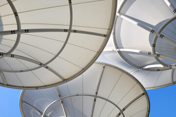 Low angle view huge canopies tensile membrane structure against sunny blue sky. - obrazy, fototapety, plakaty