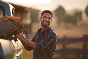 Man Loading Backpack Into Pick Up Truck For Road Trip To Cabin In Countryside