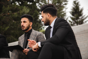 A group of business people meet outdoors. Male employees in suits communicate outdoors. Business partners discuss and argue. Relationships and promotion. Teamwork and friendship