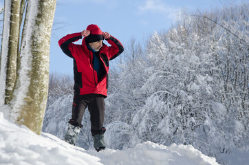 a man taking a walk in the snowy forest puts on his jacket while resting