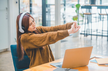 young student wearing headphones pretends to relieve fatigue during long online classes, distance learning, and keeps up to date on the global coronavirus pandemic.