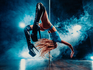 Young woman pole dancer doing flip in dark studio with smoke, tattoo on body