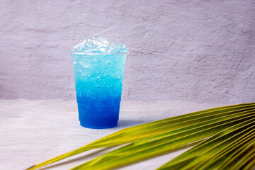 Blue Hawaiian drink in a plastic glass and coconut leaves.