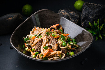 Asian udon noodles with teriyaki beef and vegetables: red pepper, tomatoes, onion and sesame seeds in a bowl.