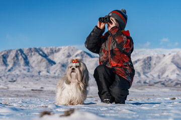 Child with binoculars and shih tzu dog posing on mountains background at winter