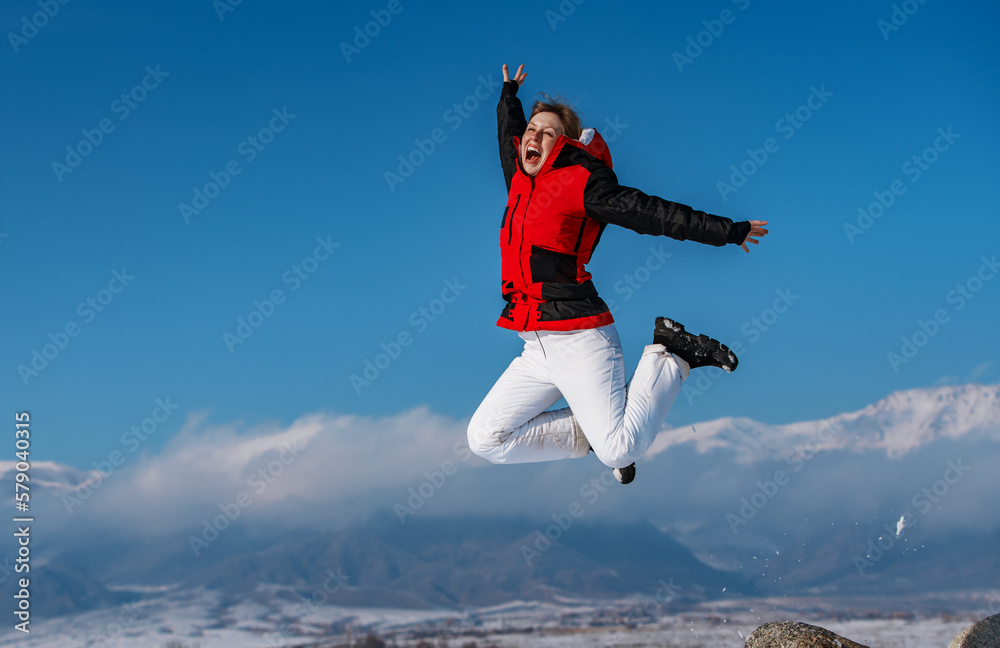 Wall mural Young happy woman jumping on mountains background in winter season