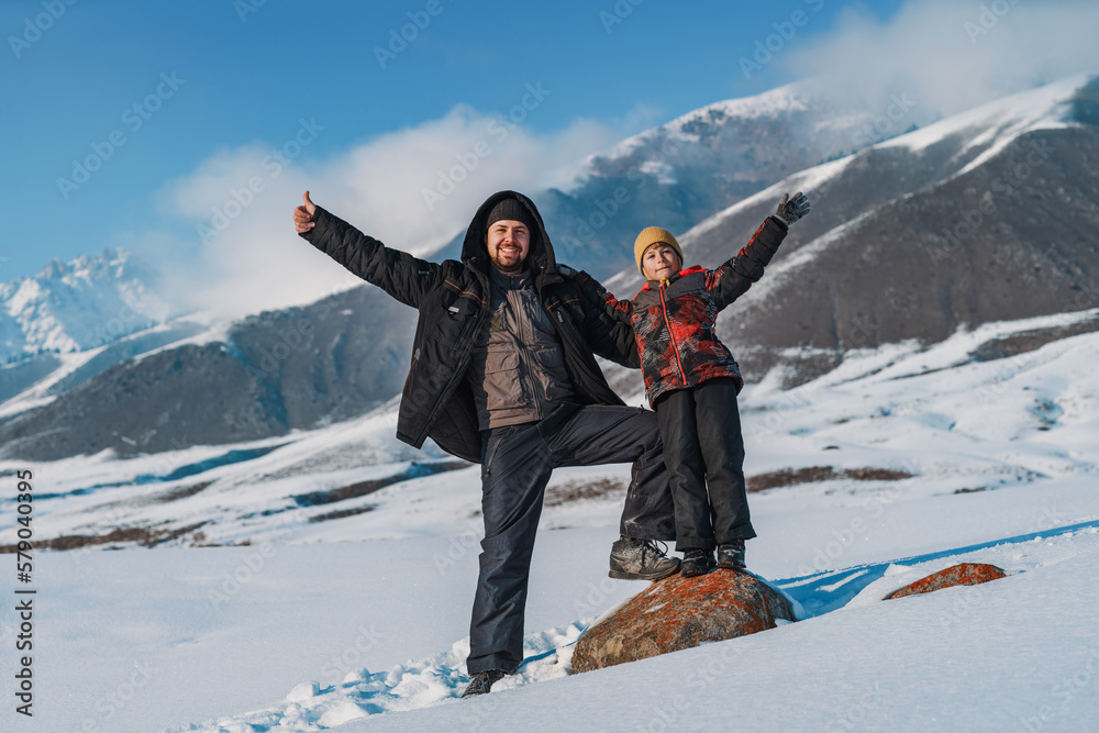 Wall mural Happy father and child waving hands and standing on mountains background at winter season