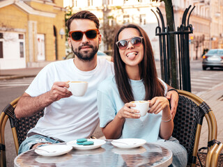 Smiling beautiful woman and her handsome boyfriend. Happy cheerful family. Couple drinking coffee in restaurant. They drinking tea at cafe in street. Holding cup. Enjoying their date. Show tongue