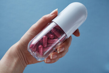 Giant capsule container filled with pink capsules in hand