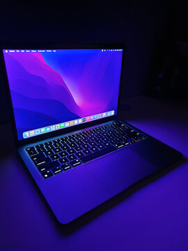 Apple MacBook Air M1 Chip Laptop with lid open on a table lit with colorful purple and blue desktop screen wallpaper in a dark room on March 8, 2023 Dubai, United Arab Emirates