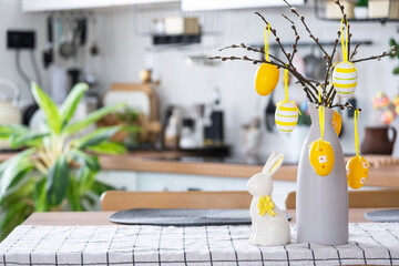 Easter decoration of colorful eggs in a basket and a rabbit on the kitchen table in a rustic style....
