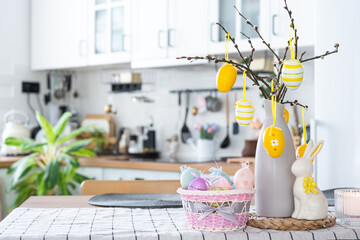 Easter decoration of colorful eggs in a basket and a rabbit on the kitchen table in a rustic style. Festive interior of a country house