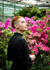  portrait of a red-haired beautiful slim girl with short hair in a tropical botanical garden in a black gothic dress with spring azalea flowers