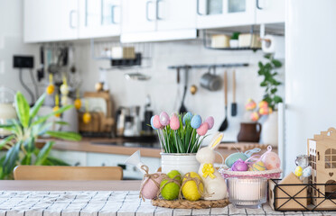 Easter decoration of colorful eggs in a basket and a rabbit on the kitchen table in a rustic style. Festive interior of a country house