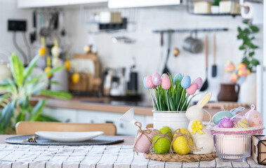 Easter decoration of colorful eggs in a basket and a rabbit on the kitchen table in a rustic style. Festive interior of a country house