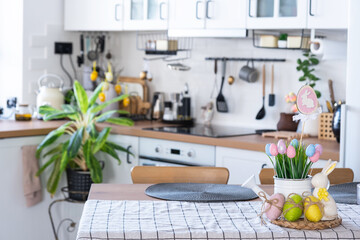 Easter decoration of colorful eggs in a basket and a rabbit on the kitchen table in a rustic style. Festive interior of a country house